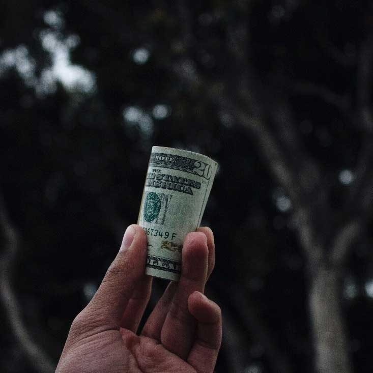 hand holding roll of twenty dollar bills for a donation